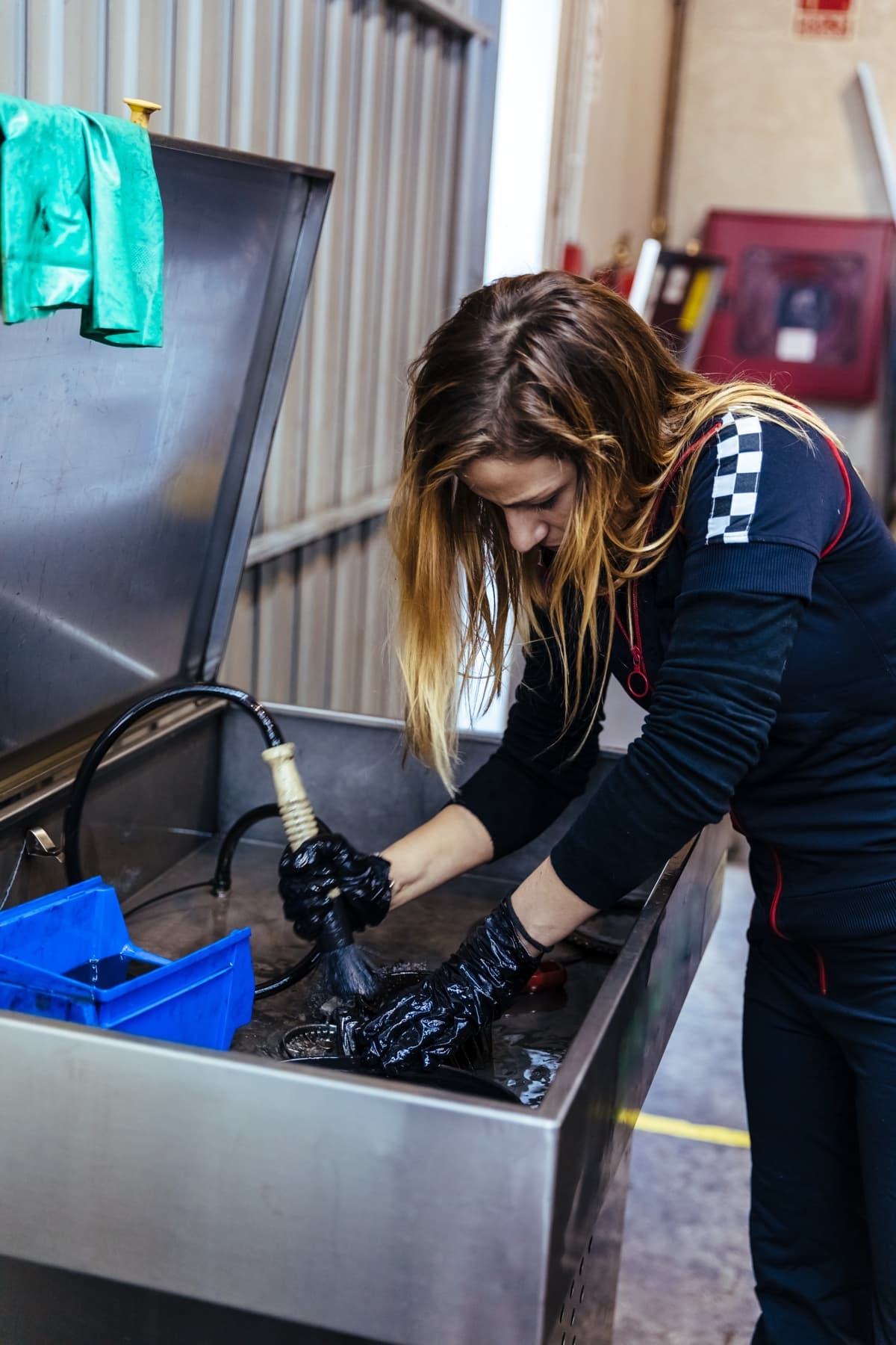 Worker degreasing a metal part in a sink-style parts washer at a mechanical workshop bench