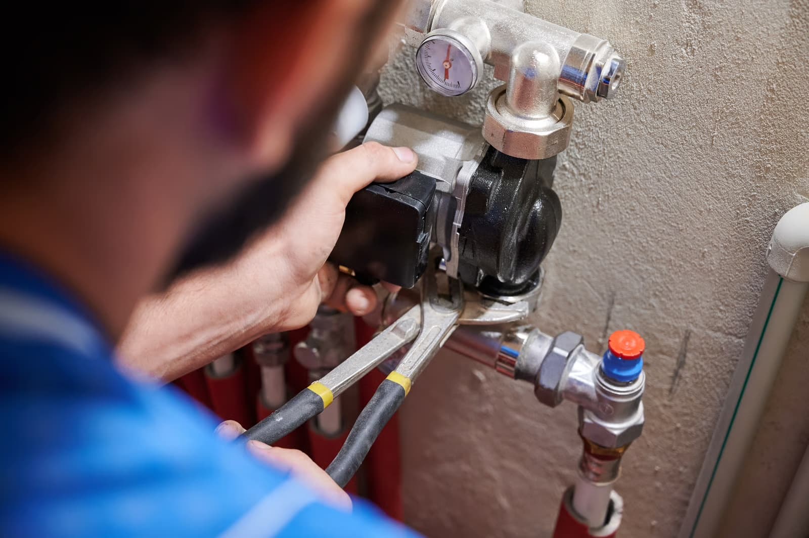 Plumber servicing a wall-mounted valve assembly with a pressure gauge and test ports in a mechanical room